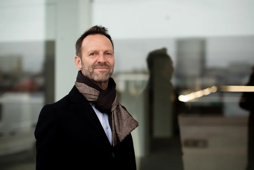 Q-Interline CEO Martin R. Henriksen press photo, scarf standing at window